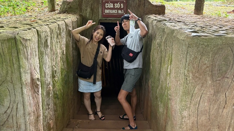 A tourist holding a brochure while asking questions to a local guide during a Hue DMZ Tour, with historic Vietnam War sites in the background.